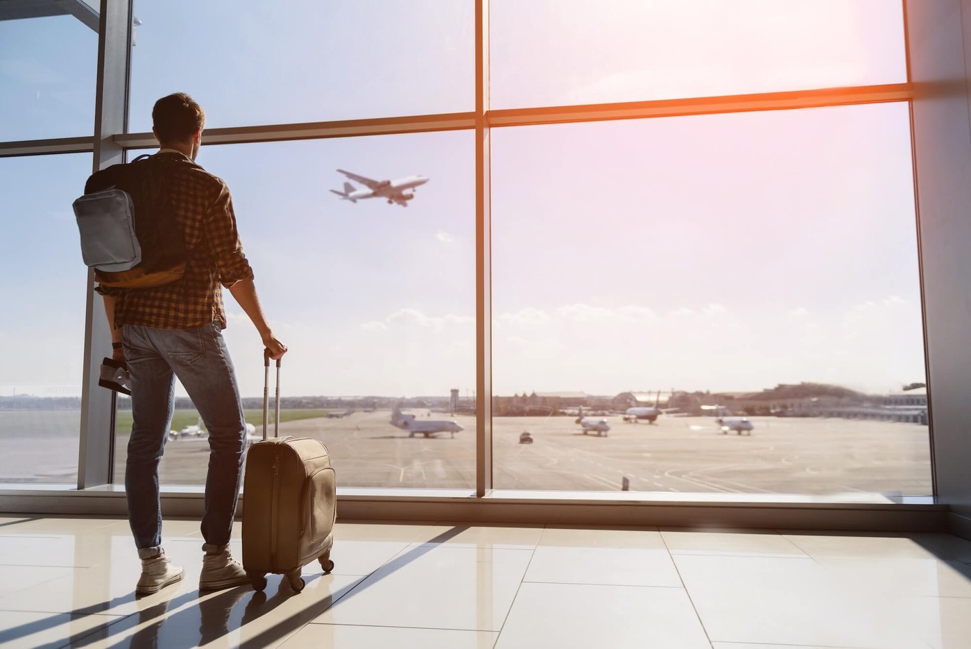 A happy passenger looks our towards an airplane flying in the sun-drenched sky