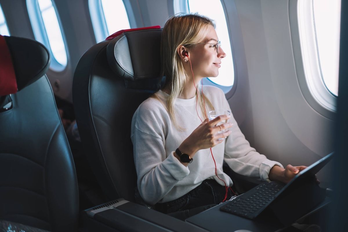 A woman sitting on the plane with a laptop and glass of water
