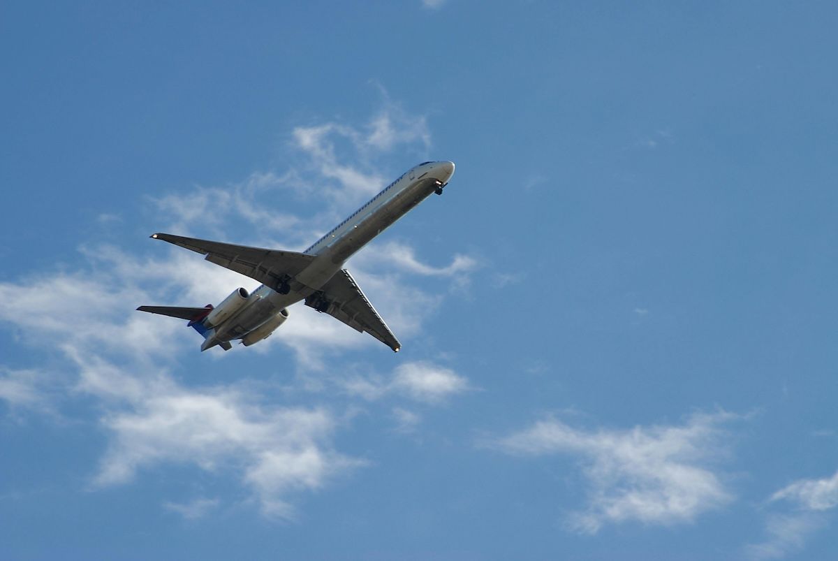 Plane flying upwards with blue sky and couple of clouds