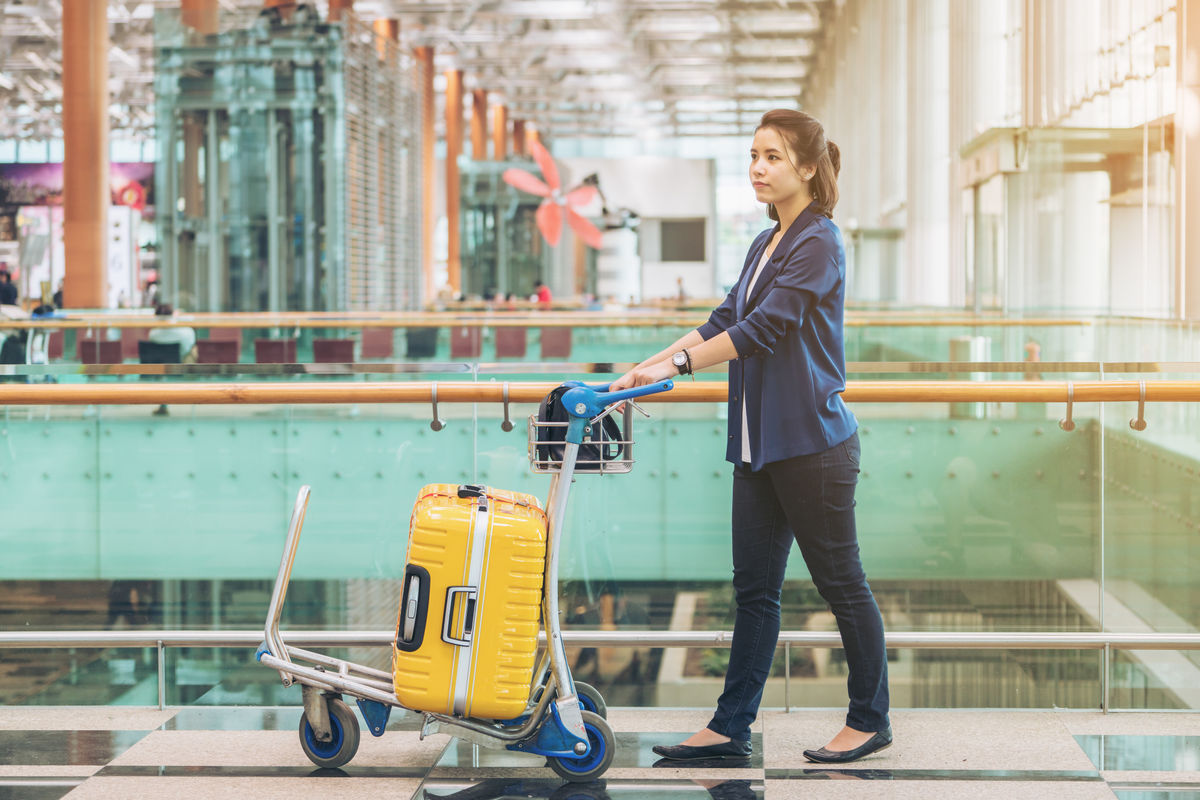 A woman is at the airport with a bright yellow suitcase