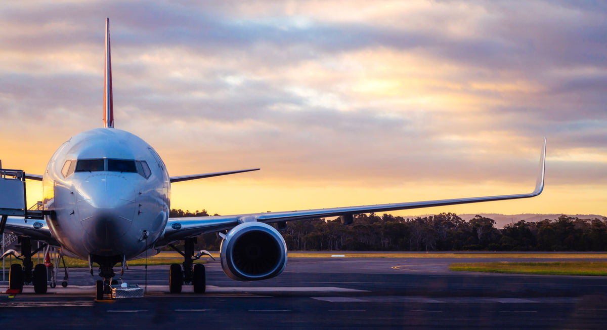 An airline waits on the runway with an orange sunset in the background