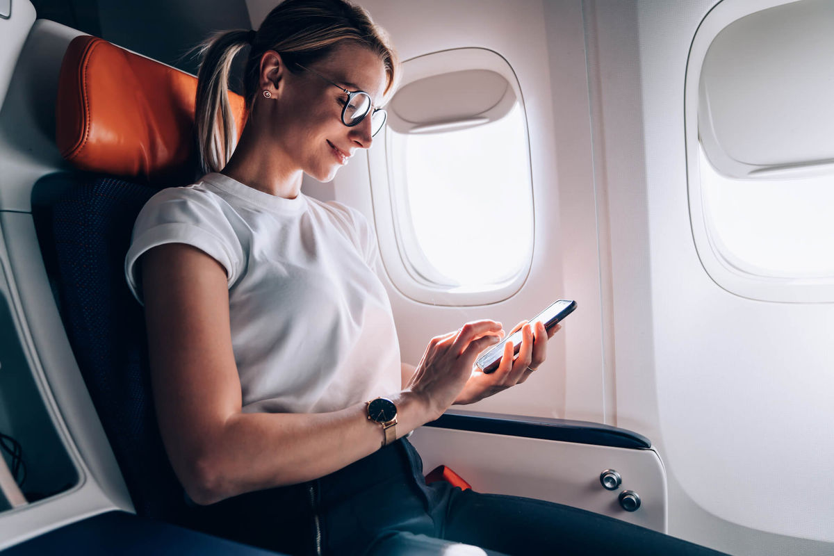 Smiling woman sitting on a plane with her phone