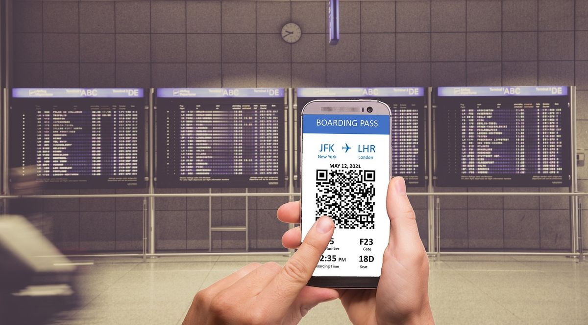 A person holds up a phone with his boarding pass in front of the airport departures board.