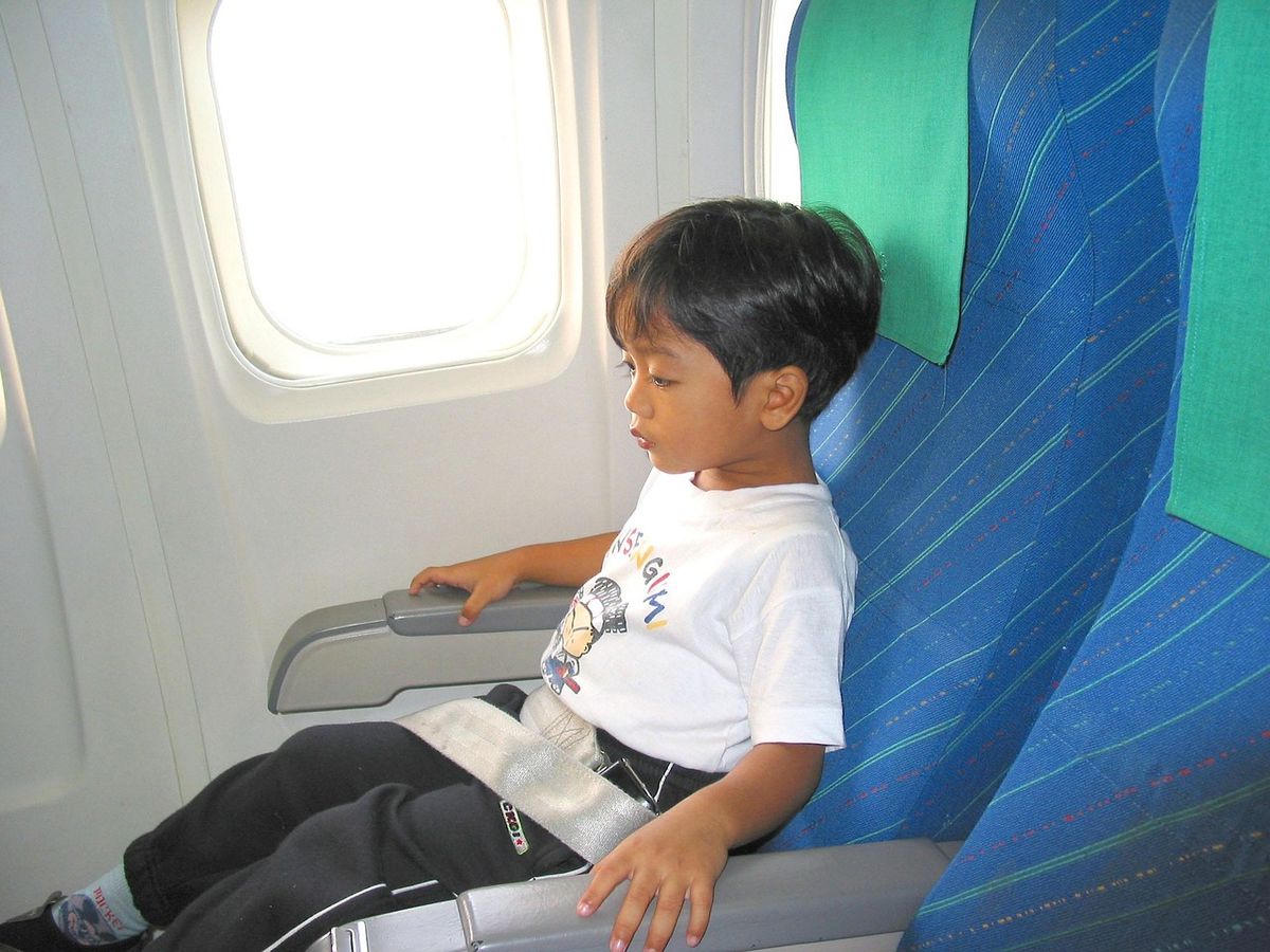 Child sitting in an aircraft seat by the window.