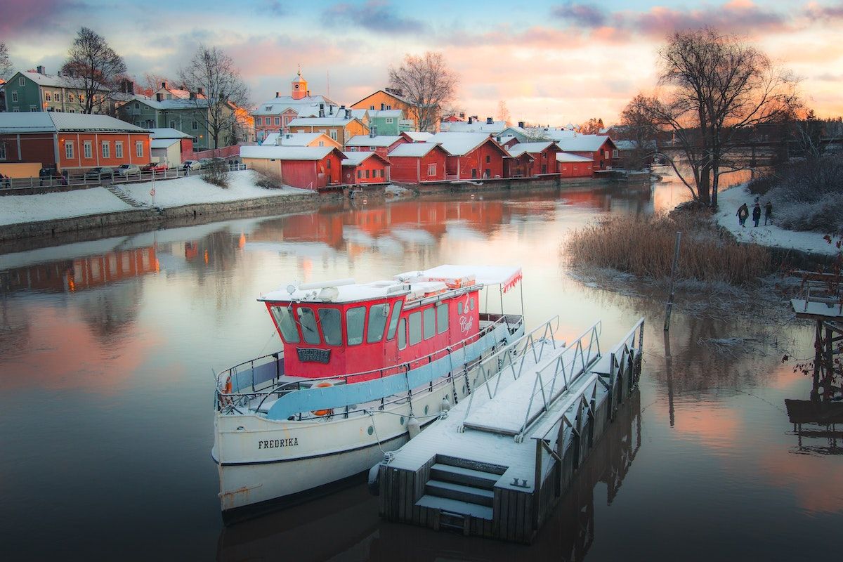 River in winter in Finland. Snow covered houses and boats by the river. 