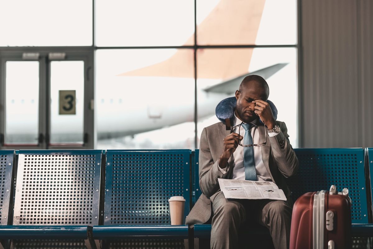 Frustrated man sitting in an airport and pinching his nose in frustration