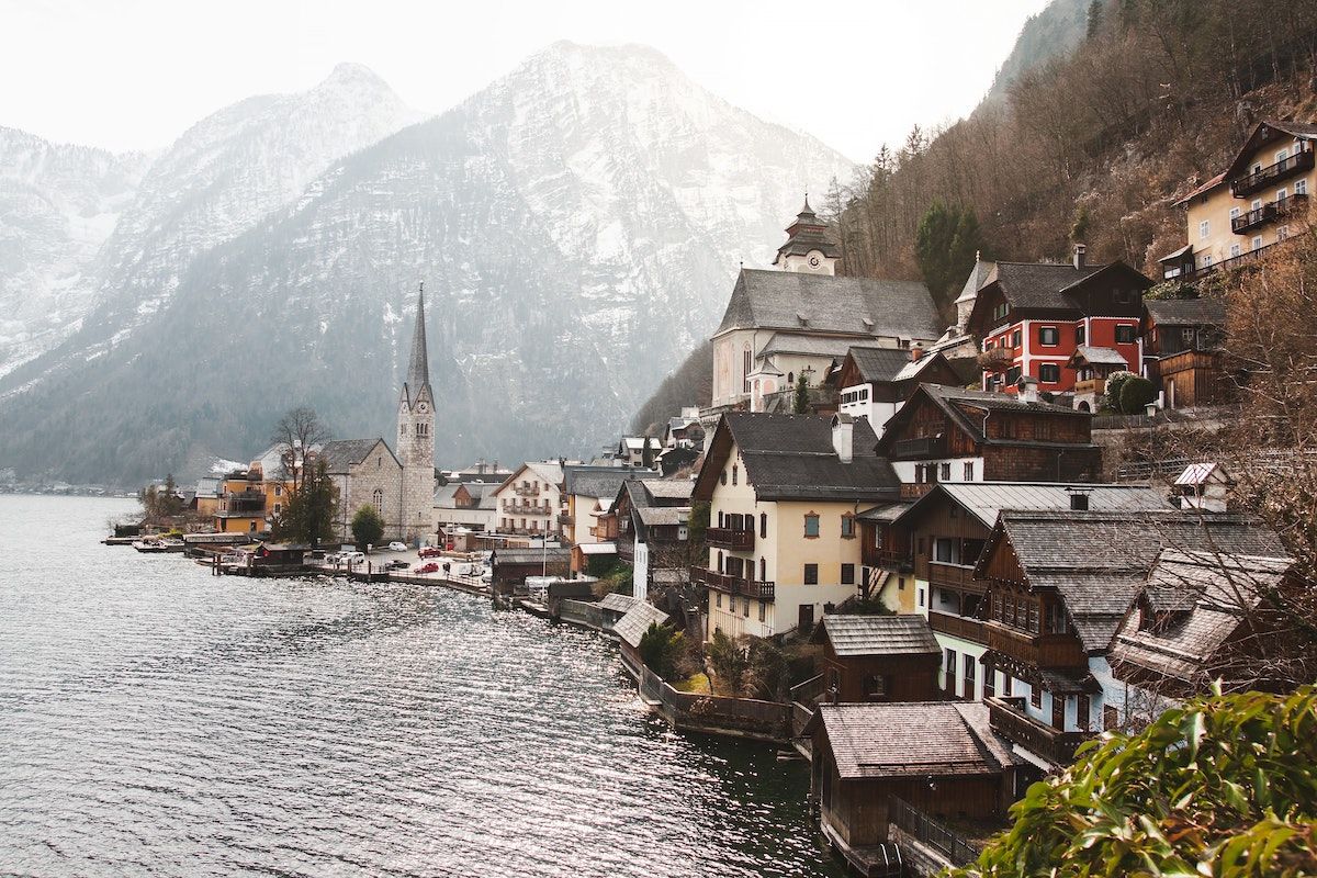 Austrian village by a body of water with snowy mountains in the background.