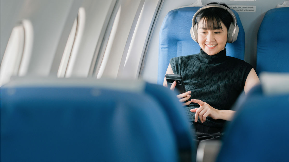 Woman sitting in the airline cabin with her phone and headphones on, looking relaxed.