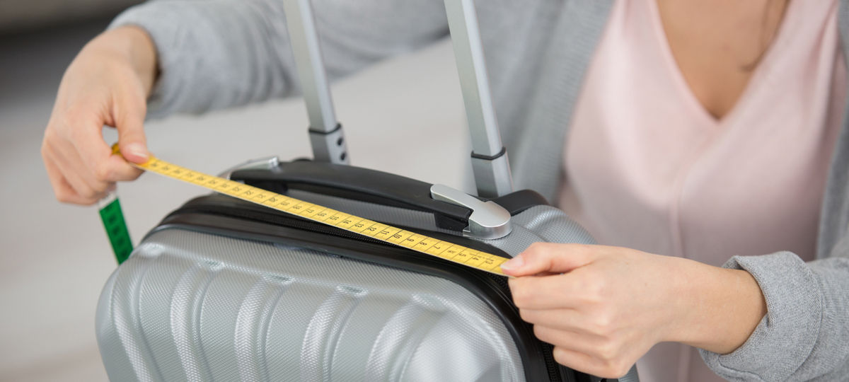 A woman uses a measuring tape to measure her luggage. 