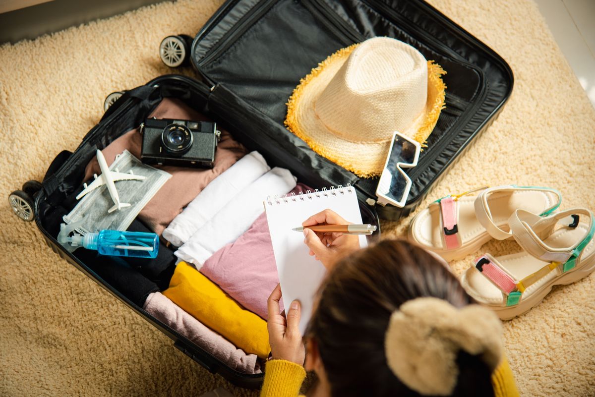 A woman writes a checklist as she packs her luggage.