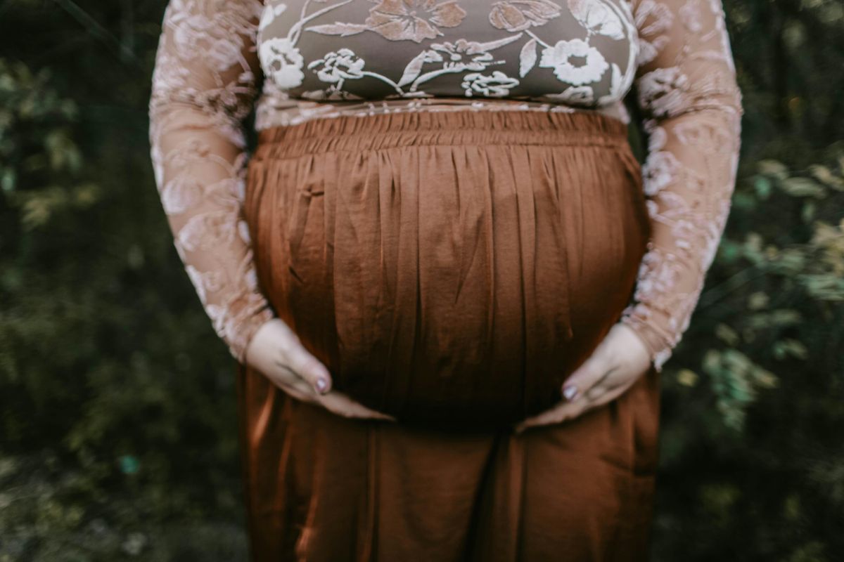 Woman in long sleeves holding her pregnant belly. 