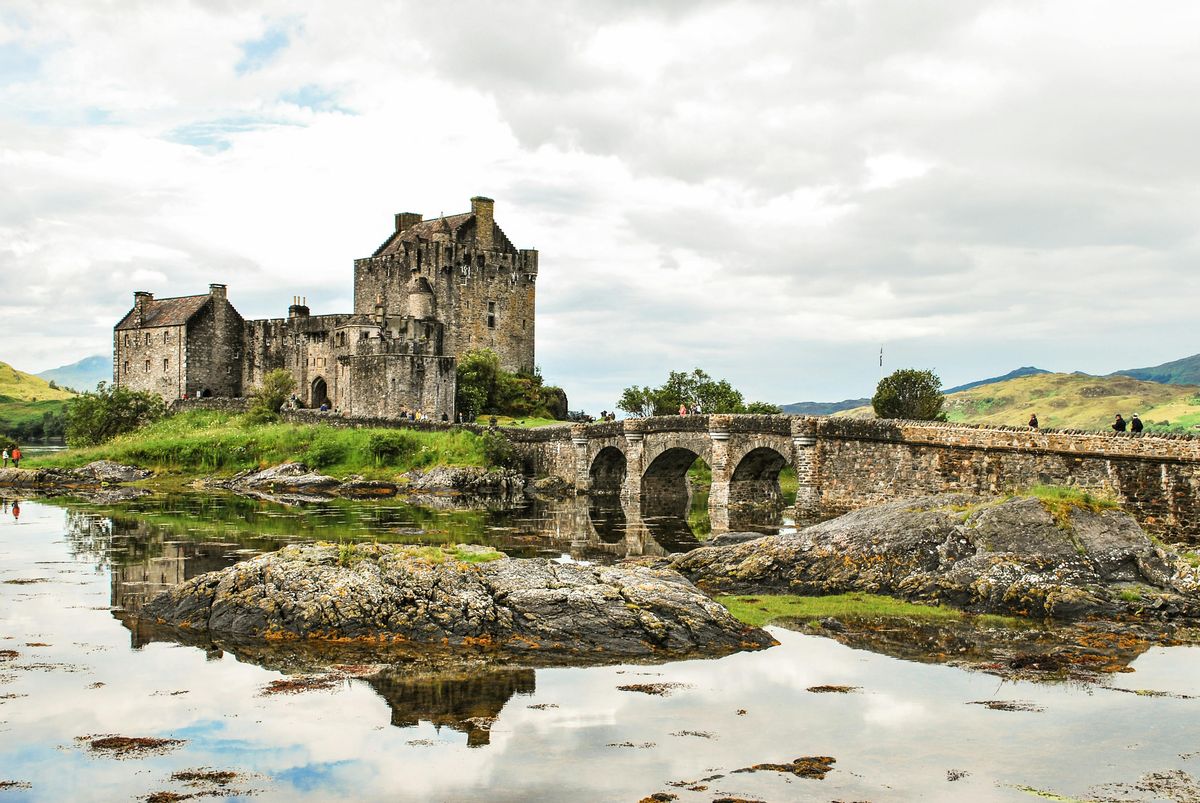 Brown brick castle in Scotland with a bridge and a pond.