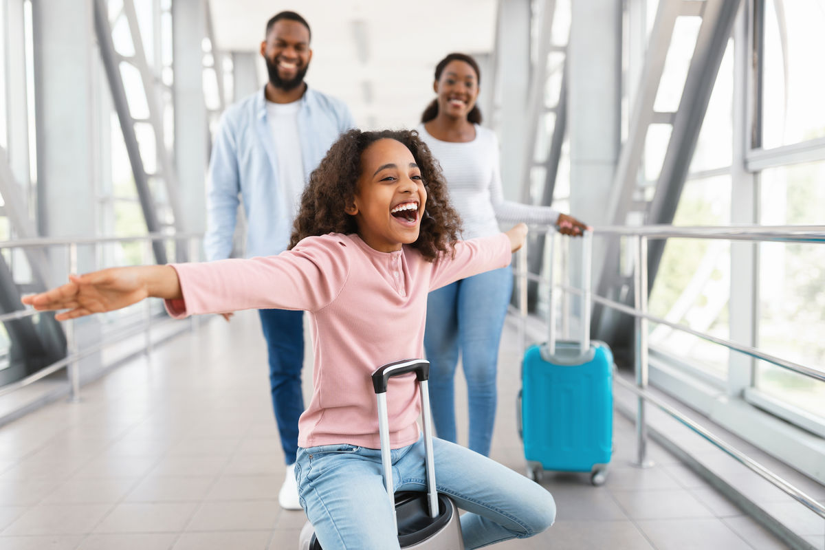 A family (dad, mum, and child) walk through a brightly lit airport terminal.