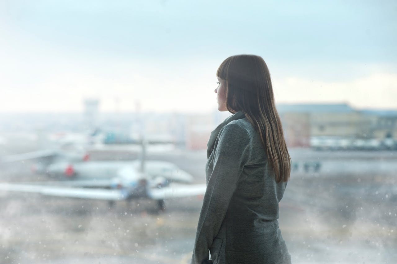 Woman stands at an airport window looking at airplanes. Gloomy atmosphere