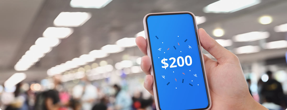 Hand holding a mobile phone showing a $200 payout from AirPayout insurance. the blurred background shows this passenger is in a busy airport