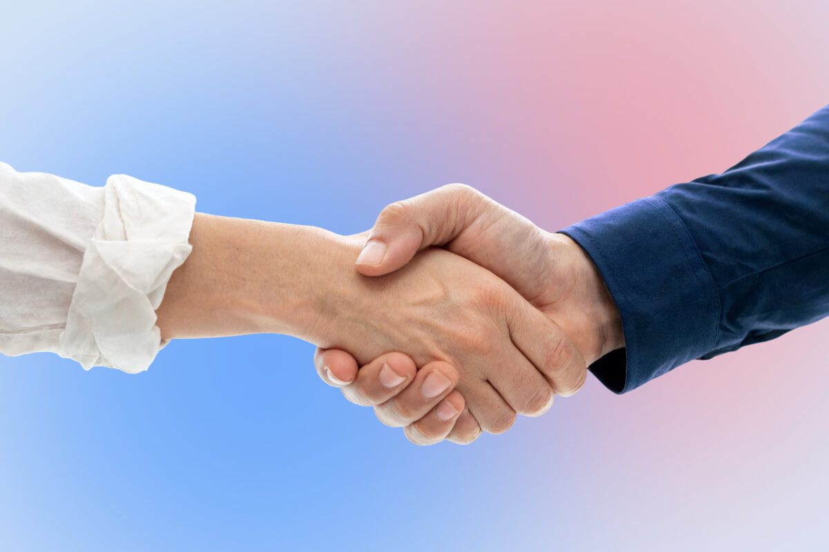 A close-up of two people shaking hands against a soft blue and pink gradient background, symbolizing a business partnership and collaboration.