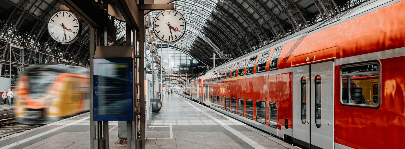 Modern trains at a major railway station platform with station clocks showing the time.