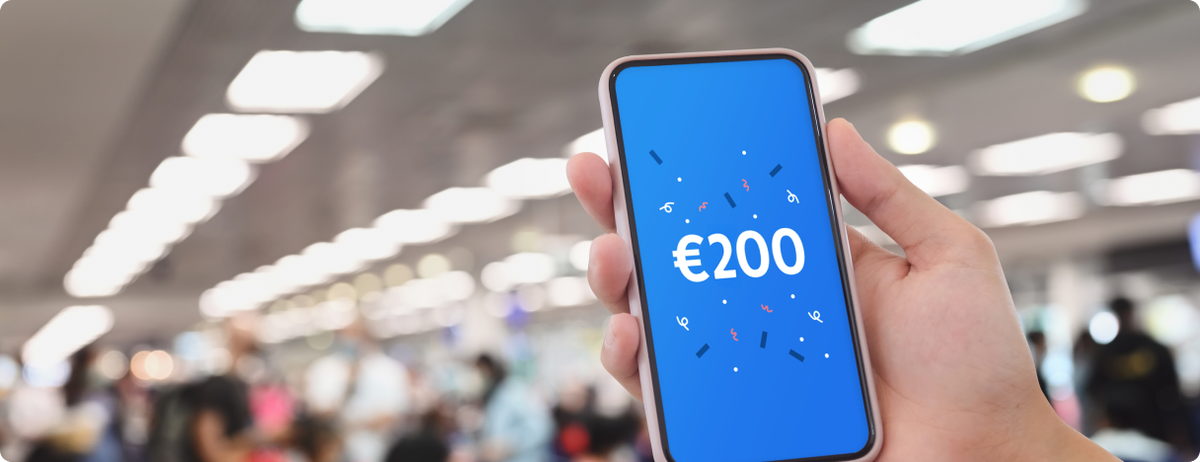 Hand holding a mobile phone showing a €200 payout from missed connection insurance. The blurred background shows this passenger is in a busy airport